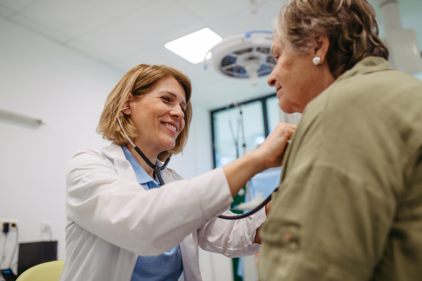 Geriatrician doctor examining elderly patient with stethoscope.. Routine health exam for elderly woman.