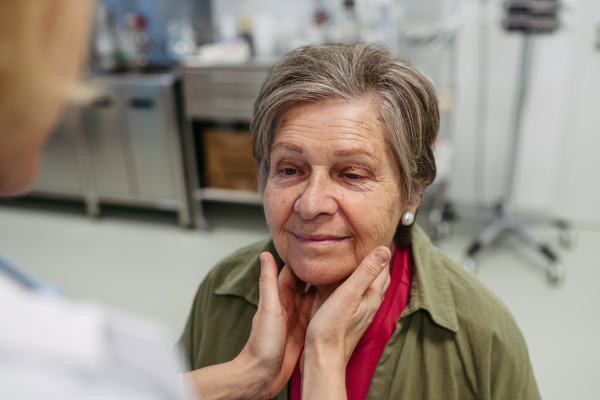 Doctor palpating lymph nodes during medical examination of senior female patient.