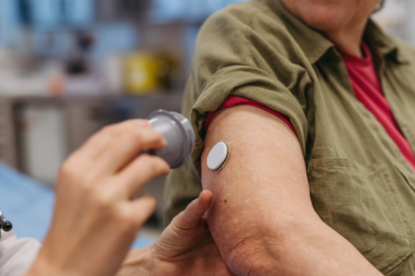 Female doctor applying CGM sensor to senior patient's arm. Medical setting.