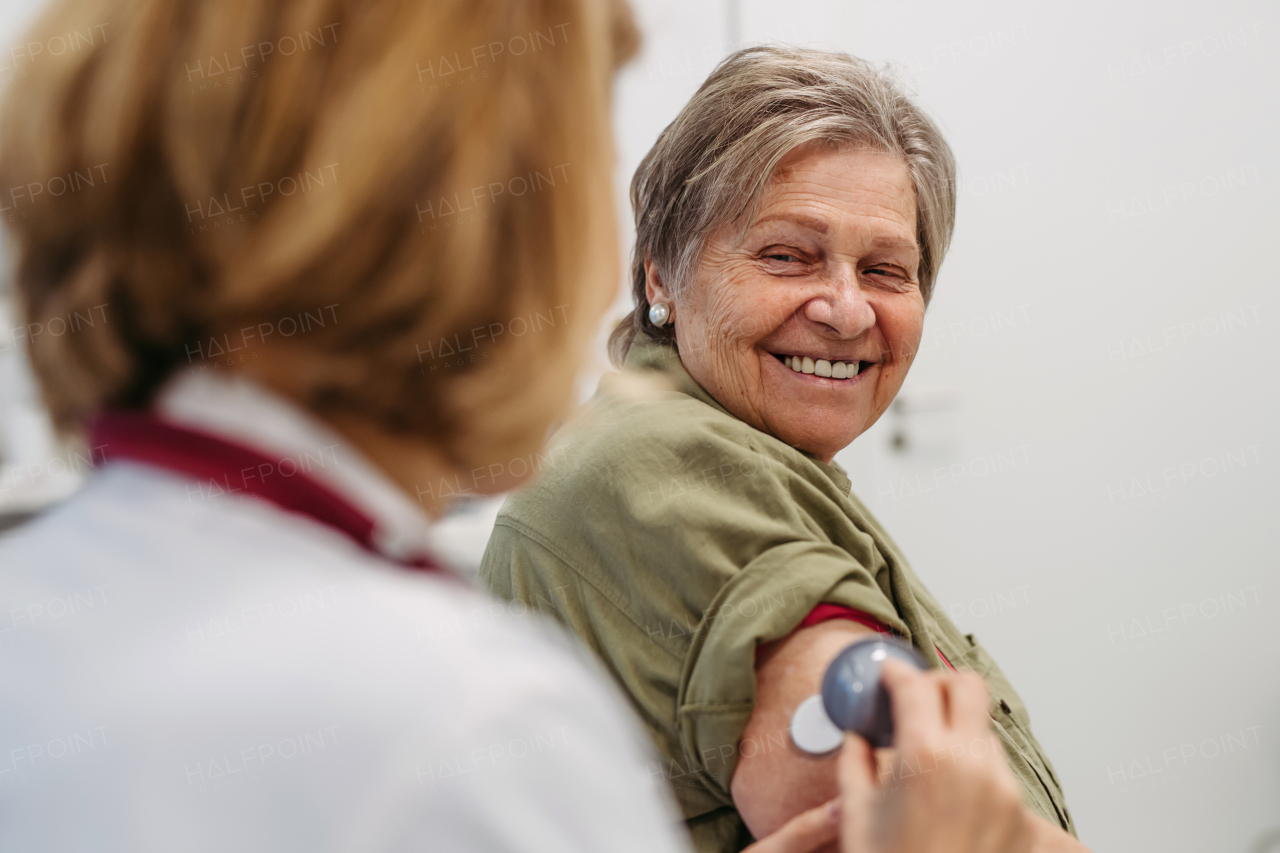 Female doctor applying CGM sensor to senior patient's arm. Medical setting.
