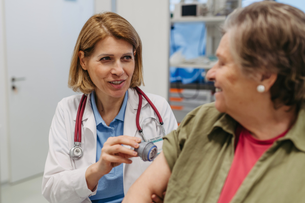 Female doctor applying CGM sensor to senior patient's arm. Medical setting.
