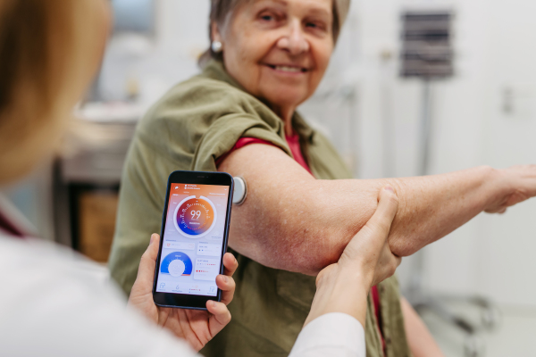 Endocrinologist teaching older patient how to connect continuous glucose monitor with mobil app. Senior health care.