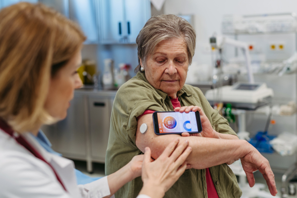Endocrinologist teaching older patient how to connect continuous glucose monitor with mobil app. Senior health care.