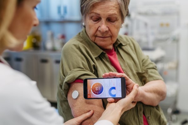 Endocrinologist teaching older patient how to connect continuous glucose monitor with mobil app. Senior health care.