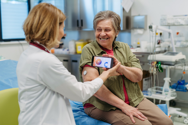 Endocrinologist teaching older patient how to connect continuous glucose monitor with mobil app. Senior health care.