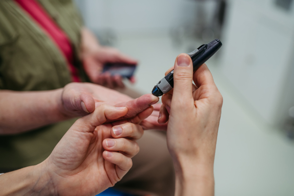 Female doctor teaching older patient how to check her blood sugar level. . Medical setting.