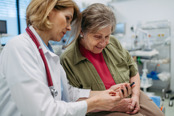 Female doctor teaching older patient how to check her blood sugar level. . Medical setting.