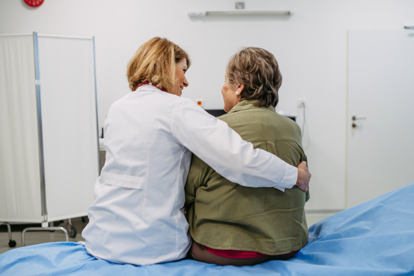 Rear view of elderly patient and female doctor in examination room. Senior health care.