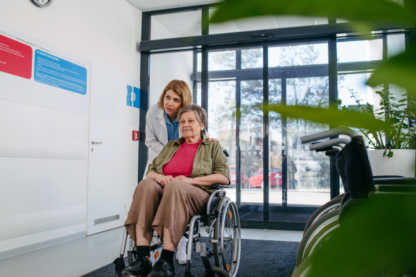 Elderly patient in wheelchair and female physician smiling at clinic. Senior health care.