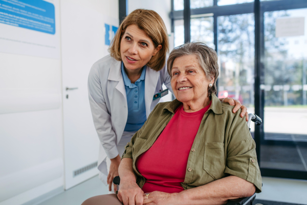 Elderly patient in wheelchair and female physician smiling at clinic. Senior health care.