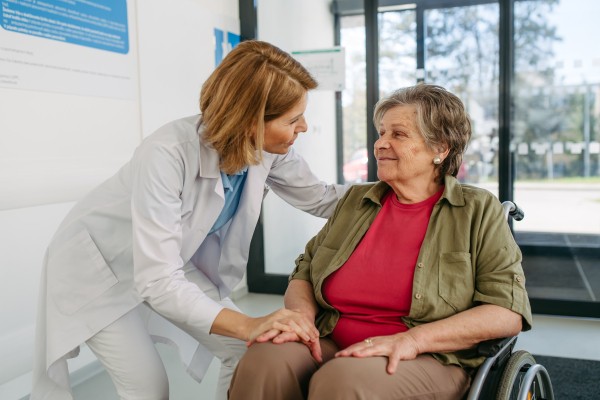 Geriatric doctor talking with patient in a wheelchair in hospital hallway. Senior health care.