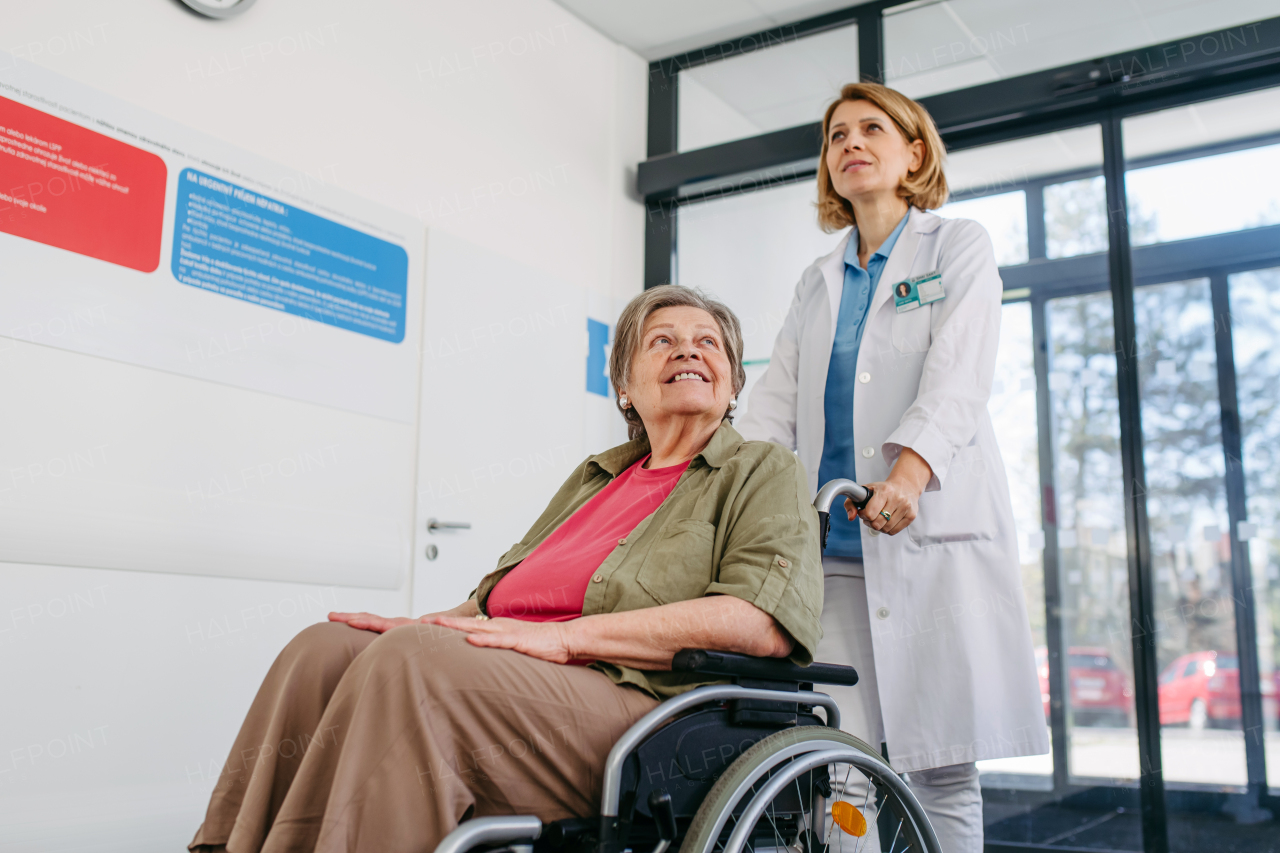 Geriatric doctor pushing a patient in a wheelchair down a hospital hallway. Senior health care.