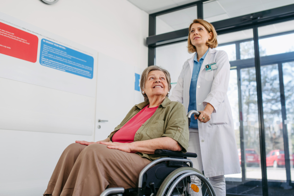 Geriatric doctor pushing a patient in a wheelchair down a hospital hallway. Senior health care.