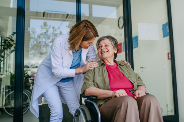 Geriatric doctor pushing a patient in a wheelchair down a hospital hallway. Senior health care.