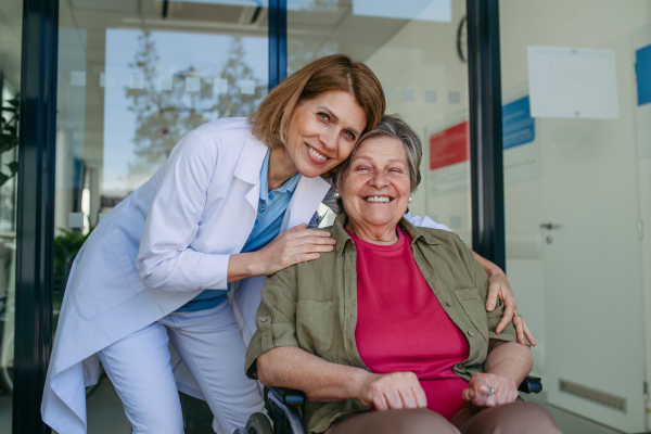 Geriatric doctor talking with patient in a wheelchair in hospital hallway. Senior health care.