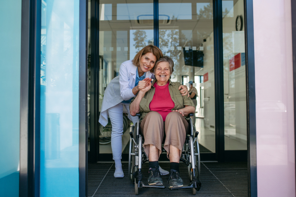 Elderly patient in wheelchair and female physician smiling at clinic. Senior health care.