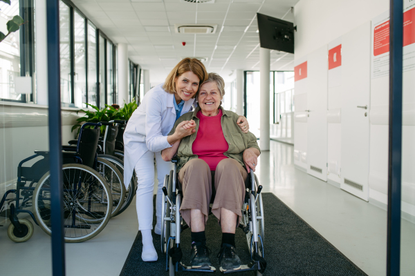 Elderly patient in wheelchair and female physician smiling at clinic. Senior health care.