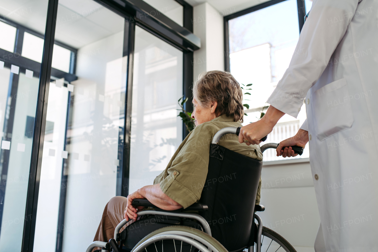 Geriatric doctor pushing a patient in a wheelchair down a hospital hallway. Senior health care.