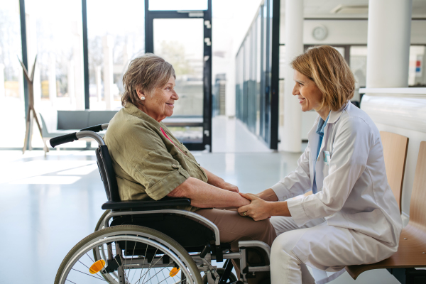 Elderly patient in wheelchair talking with female physician. Senior health care.