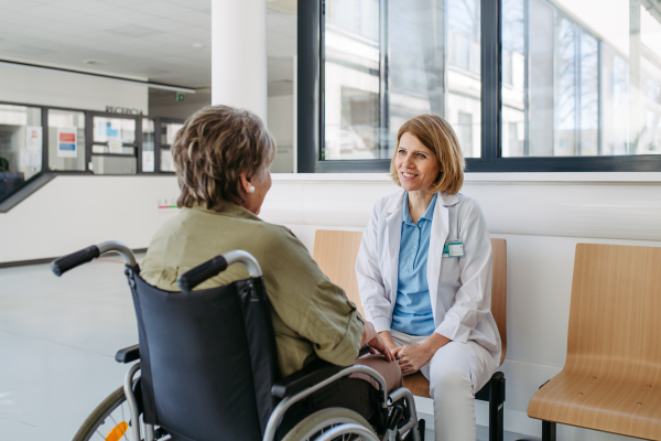 Elderly patient in wheelchair talking with female physician. Senior health care.