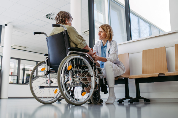 Elderly patient in wheelchair talking with female physician. Senior health care.