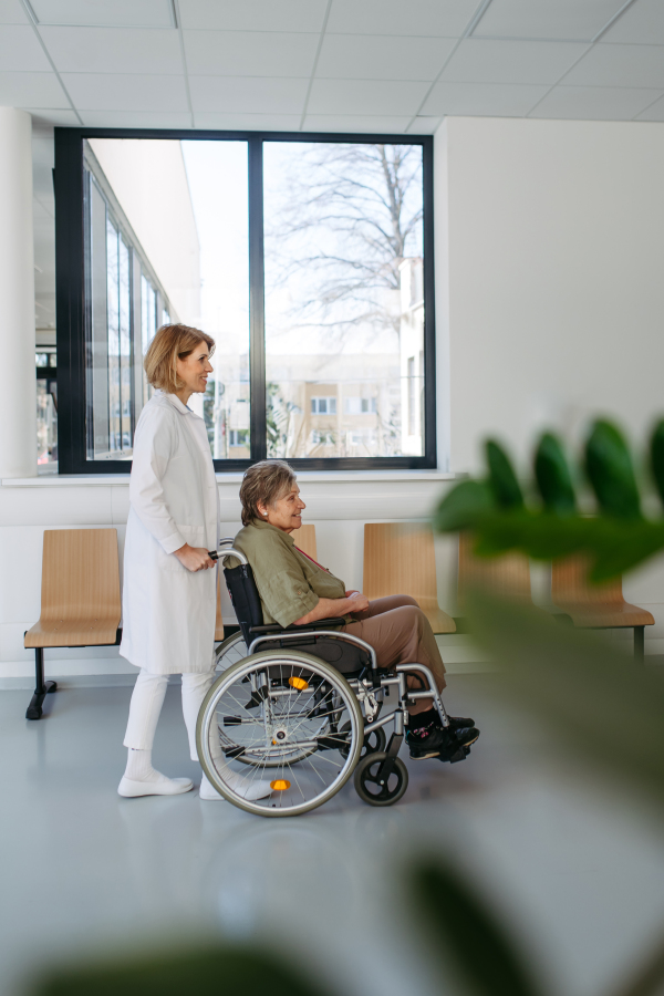 Geriatric doctor pushing a patient in a wheelchair down a hospital hallway. Senior health care.