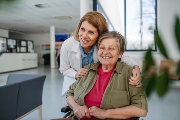 Elderly patient in wheelchair and female physician smiling at clinic. Senior health care.
