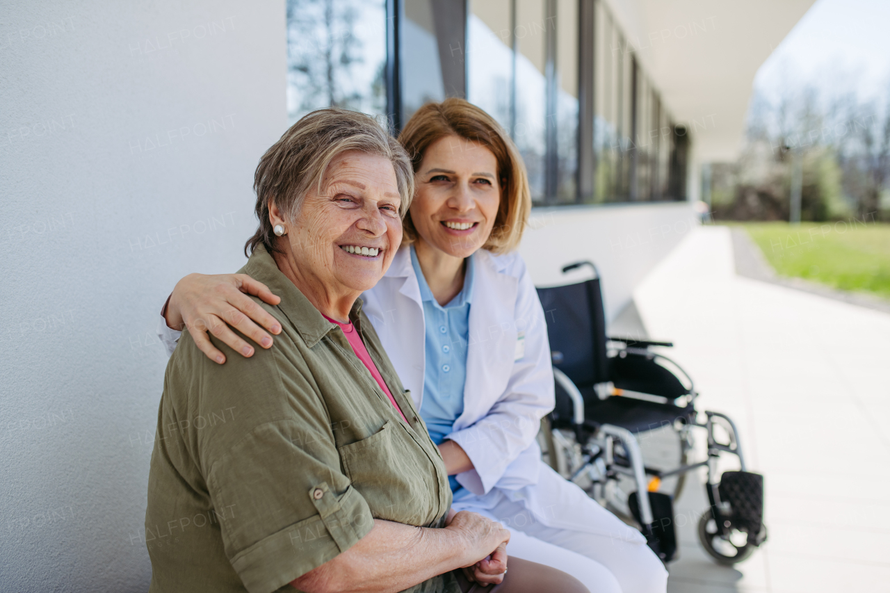 Elderly patient talking with caring female physician in front of hospital. Senior health care.