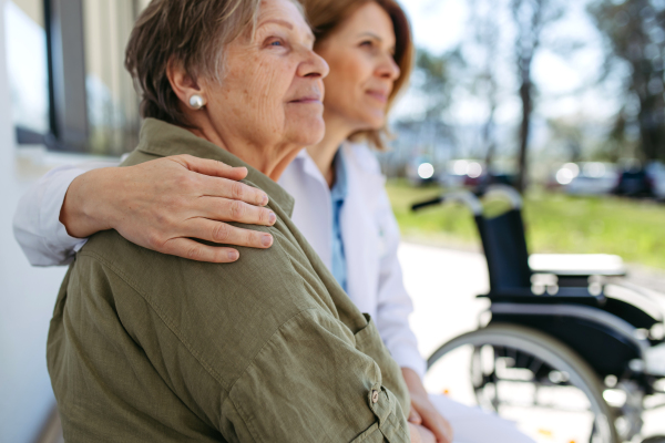 Doctor and elderly patient sitting in front of hospital building and talking. Senior health care.