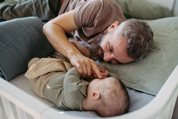 Father putting the baby to sleep, lying next to him in the crib and soothing him.