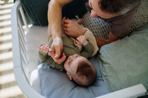 Father putting the baby to sleep, lying next to him in the crib and soothing him.