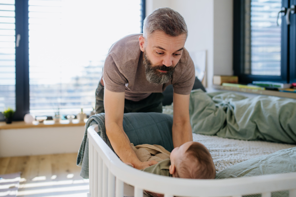 Father putting the baby to sleep, lying him down in crib., soothing him.