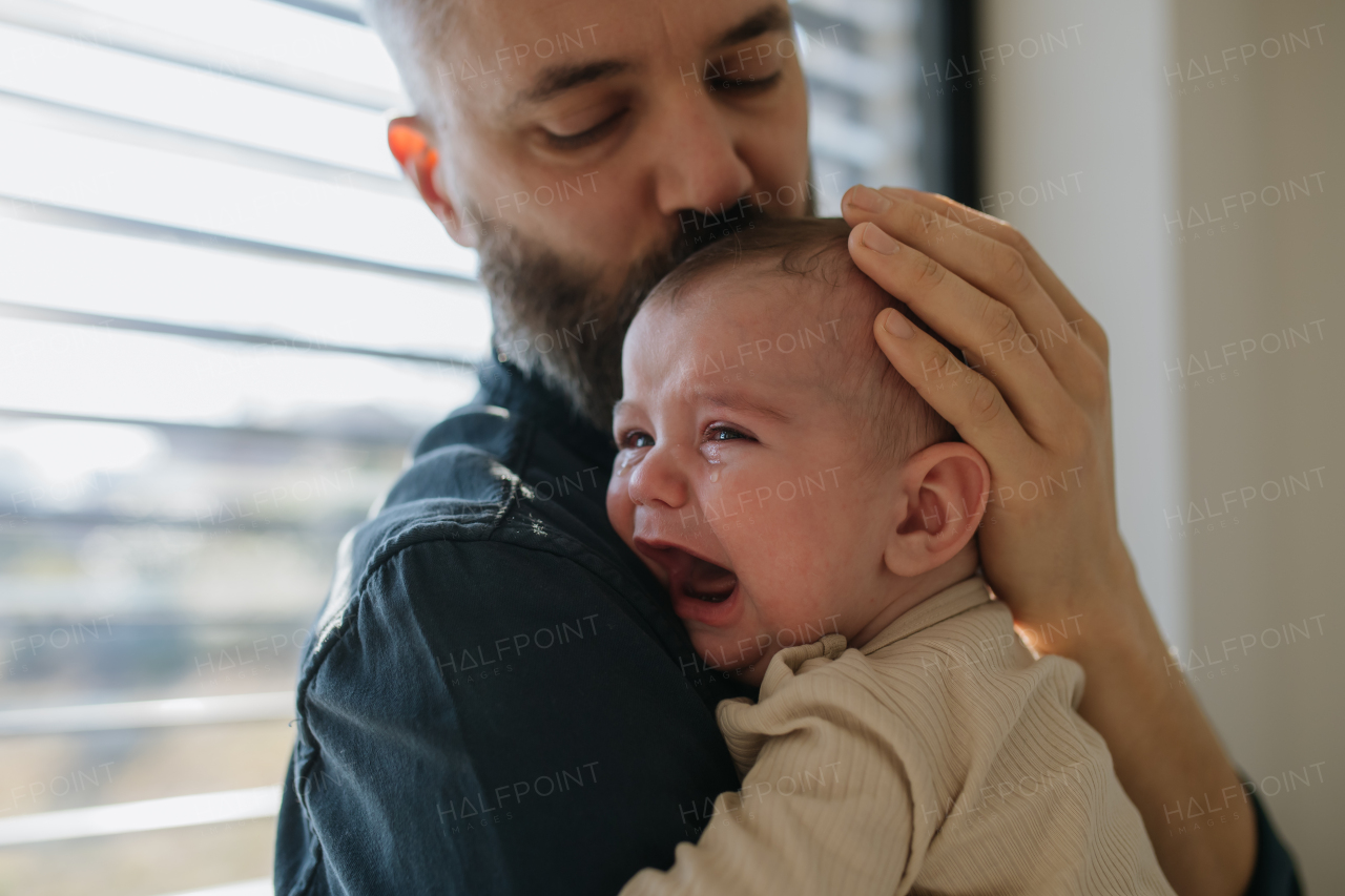 Father comforting his crying baby son, holding him in arms.
