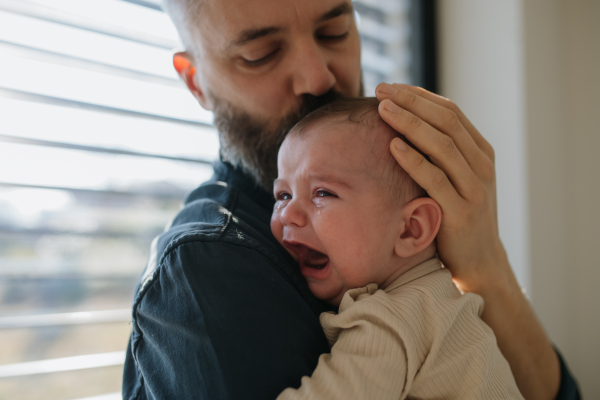 Father comforting his crying baby son, holding him in arms.