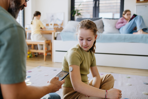 Diabetic girl with a CGM sensor on her arm. Father using an app to monitor blood sugar levels.