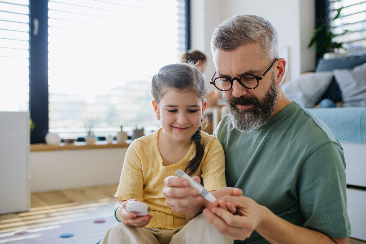 Diabetic girl taking blood sugar test at home, father helping.