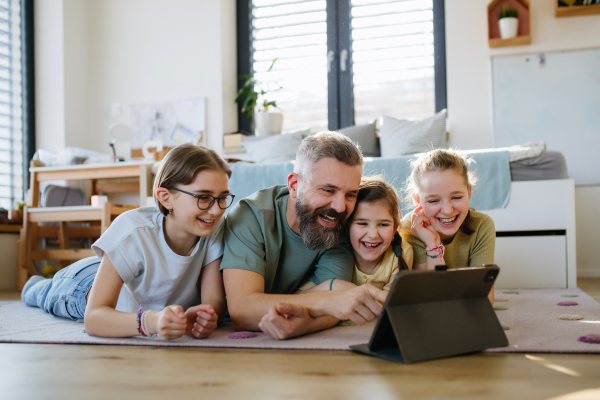 Portrait of father with three daughters watching tv show on tablet. Girl dad concept.