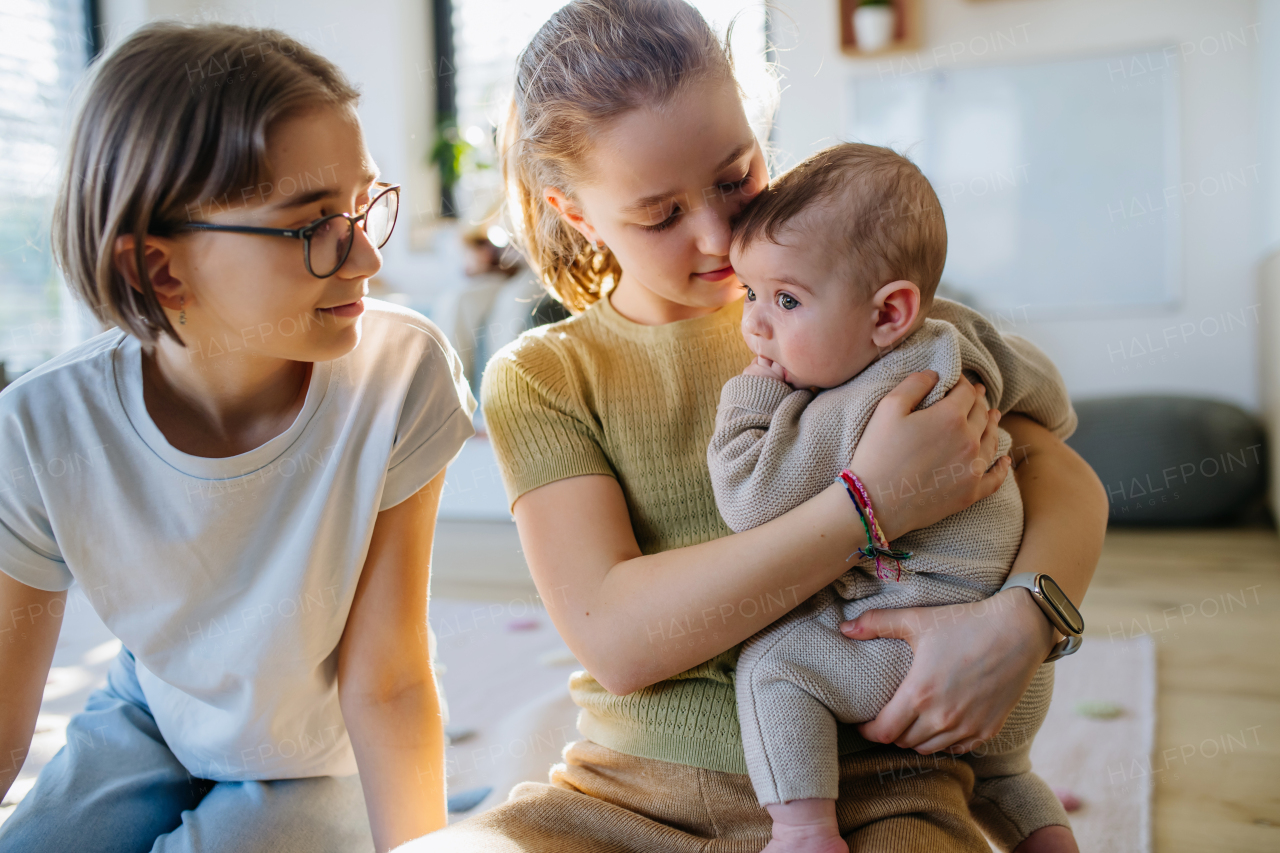 Big sisters holding small little baby brother in arms, taking care of him.
