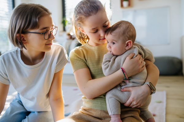 Big sisters holding small little baby brother in arms, taking care of him.