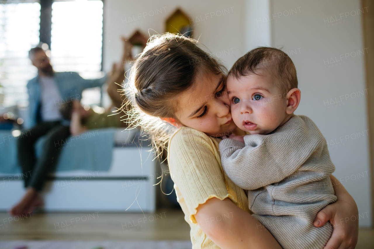 Big sister holding small little baby brother in her arms, taking care of him.
