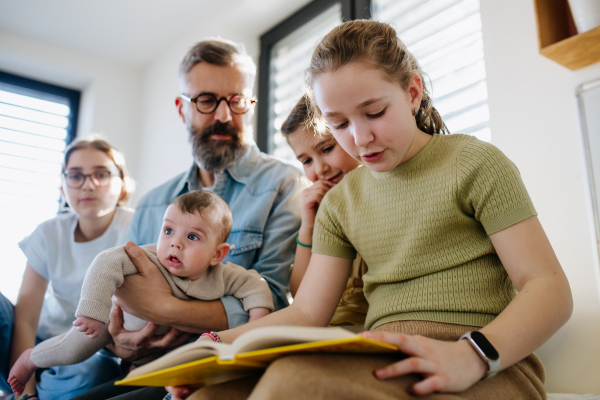 Three sisters and father taking care of newborn brother and reading book.