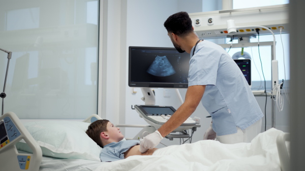 Male doctor using ultrasound probe to check on young boy, abdominal ultrasound.