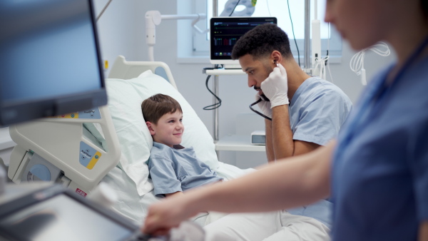 A nurse and doctor caring for young boy patient lying in hospital bed.