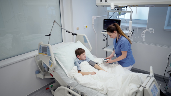 Female nurse caring for young boy patient lying in hospital bed.