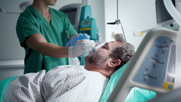 Male doctor providing oxygen ventilation to unconscious patient in hospital.