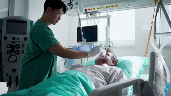 Male doctor providing oxygen ventilation to unconscious patient in hospital.