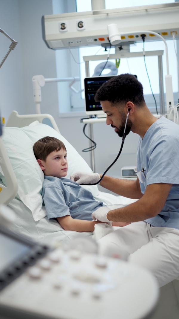 Young male doctor using a stethoscope, listening to breathing and heartbeat of boy patient.