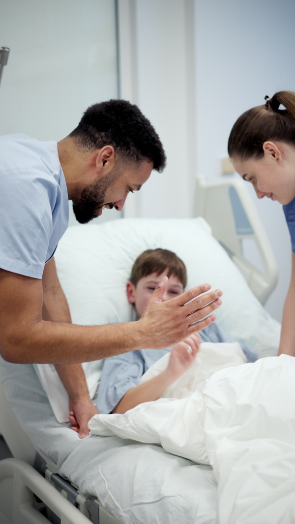 A nurse and doctor caring for young boy patient lying in hospital bed.
