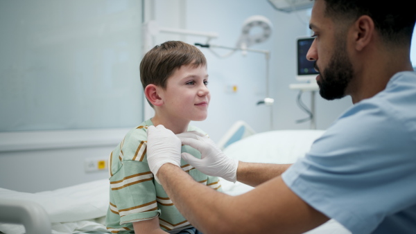 Male doctor examining young boy patient sitting on hospital bed.