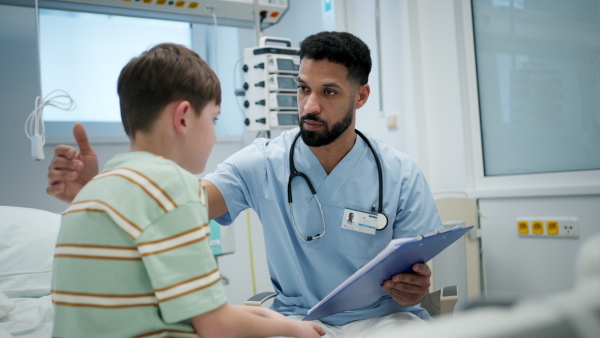 Male doctor examining young boy patient sitting on hospital bed.